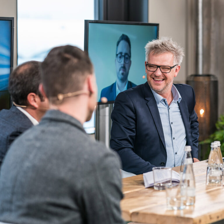 Holger Erdrich moderiert eine Podiumsdiskussion und lacht herzlich mit den Gesprächspartnern bei der SAP connect 2021 im Speicher7 in Mannheim