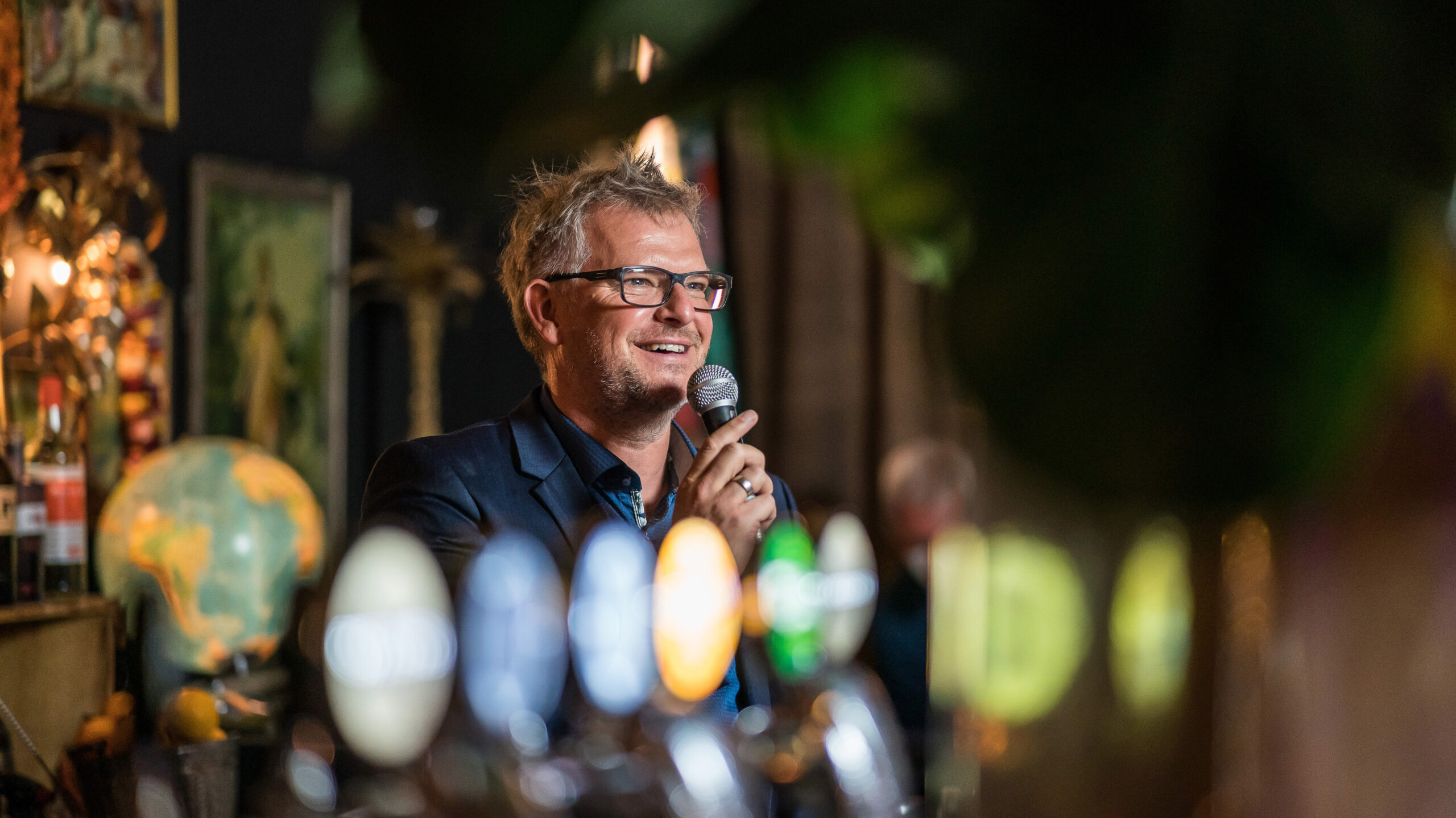 Holger Erdrich moderiert mit Handmikrofon bei einem Abendempfang in entspannter Atmosph&auml;re an einer Bar