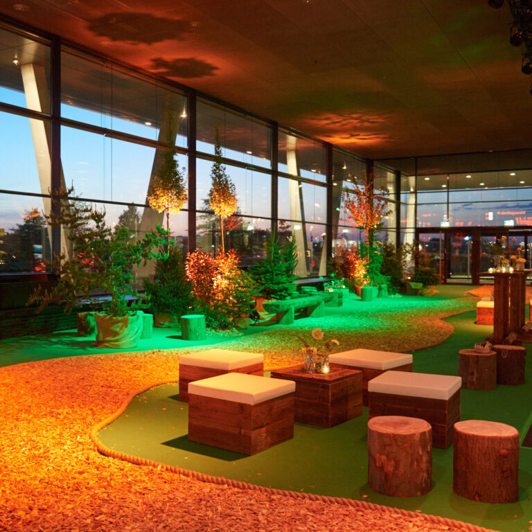 Aufwändig gestalteter Event-Bereich als Waldkulisse mit Bäumen, Baumstümpfen und warmem Licht